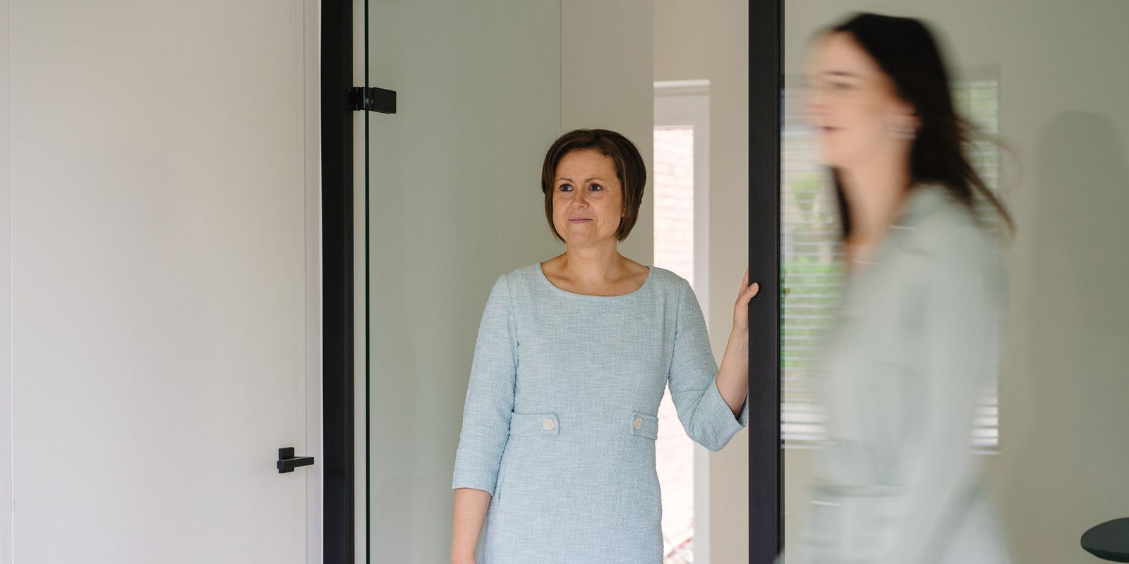 Advocaat Tina Devlamynck staat in een deuropening terwijl advocaat Helena Debaere voorbij wandelt.